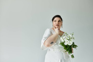 Göz kamaştırıcı, büyük beden bir gelin beyaz bir elbise içinde zarif bir şekilde poz verir ve elinde bir buket ile zarafet saçar..