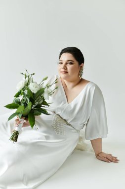 Göz kamaştırıcı bir gelin, beyaz bir elbiseyle, zarif bir şekilde oturmuş, elinde çiçek buketi ile güzel bir ışık saçar..