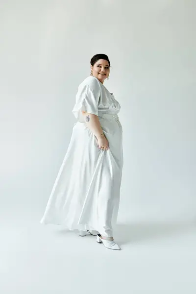 stock image A stunning bride radiates joy in a flowing white gown, accented by elegant earrings, set against a muted grey background.