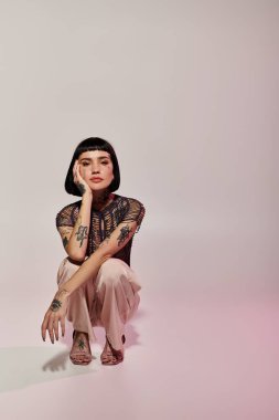 A stylish woman with tattoos kneels gracefully, showcasing her unique look and attire. clipart