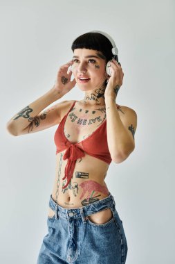 Dövmeli neşeli bir kadın modaya uygun kıyafetler giyerken müzik dinliyor..