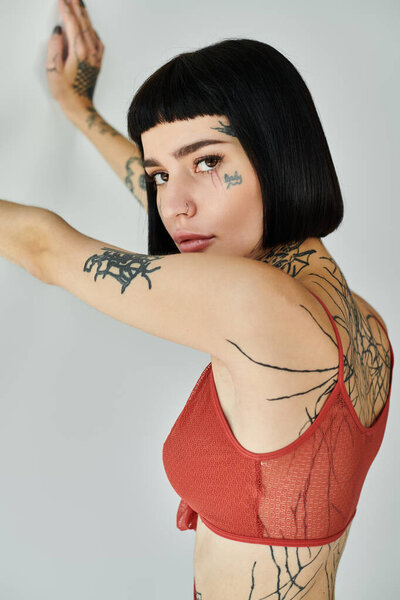 Молодая женщина демонстрирует свои татуировки, в то же время позируя в модном наряде.