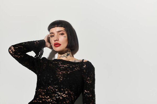 Модная женщина уверенно позирует с яркими татуировками на простом фоне.