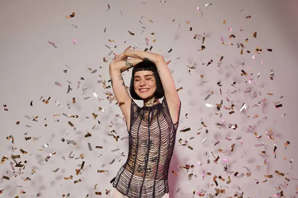 stock image A cheerful woman dances with arms raised as colorful confetti surrounds her.