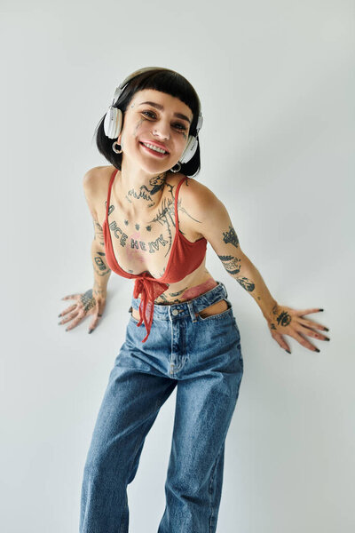 Модная женщина с татуировками с радостью позирует на светлом фоне.