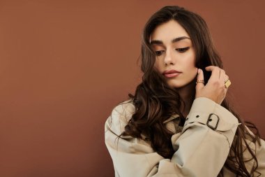 Genç bir kadın şık bir sonbahar elbisesi içinde zarif bir poz veriyor, rahat bir arkaplana karşı zarafet yayıyor..