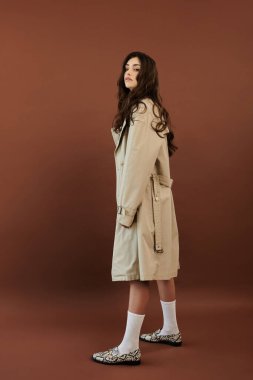 Şık bir genç kadın zarif bir sonbahar elbisesi içinde poz verir. Sıcak bir stüdyo ortamında sezonluk moda trendlerini somutlaştırır..