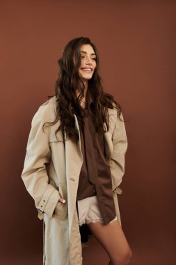 Genç bir kadın, rahat bir stüdyo ortamında sıcacık ve tarz saçan bir sonbahar kıyafetinin içinde güven içinde poz veriyor..