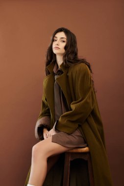 Genç bir kadın, şık bir stüdyoda, mevsimsel zarafeti somutlaştıran modaya uygun bir sonbahar elbisesi sergiliyor..