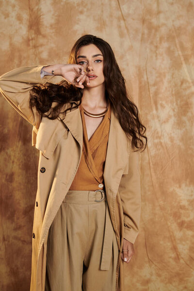 Стилизованная в модном осеннем ансамбле, молодая женщина занимает уверенную позу в уютной студии, сохраняя сезонную элегантность.