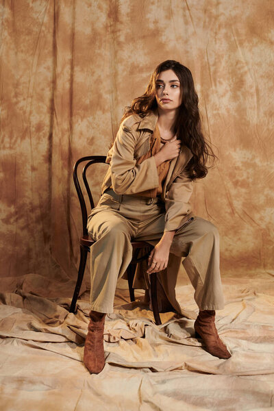 A young woman showcases a trendy autumn outfit, seated gracefully in a stylish studio setting, exuding confidence and charm.