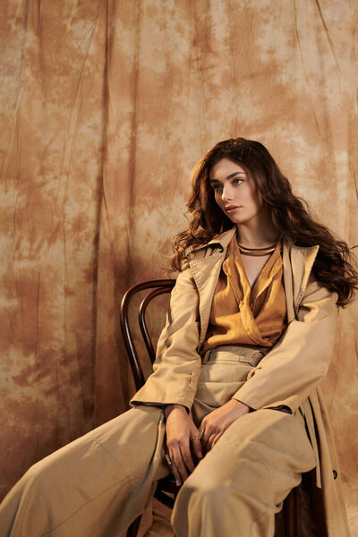 A beautiful young woman poses gracefully in an elegant autumn outfit, surrounded by warm, inviting tones.