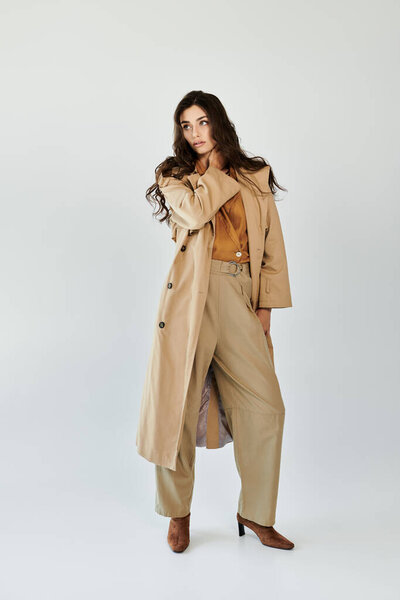 Молодая женщина моделирует шикарный осенний наряд, со стильным плащом и брюками, излучающими элегантность в студии.