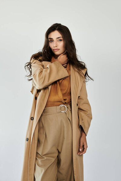 Молодая женщина демонстрирует свой осенний стиль в шикарном наряде, излучая уверенность и элегантность на минималистическом фоне.