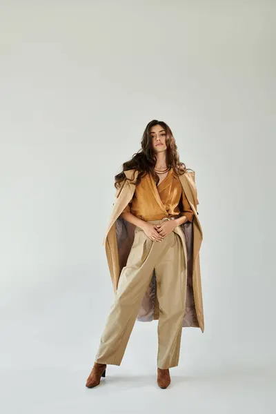 stock image A young woman exudes confidence in a fashionable autumn outfit, posing gracefully in a well-lit studio environment.