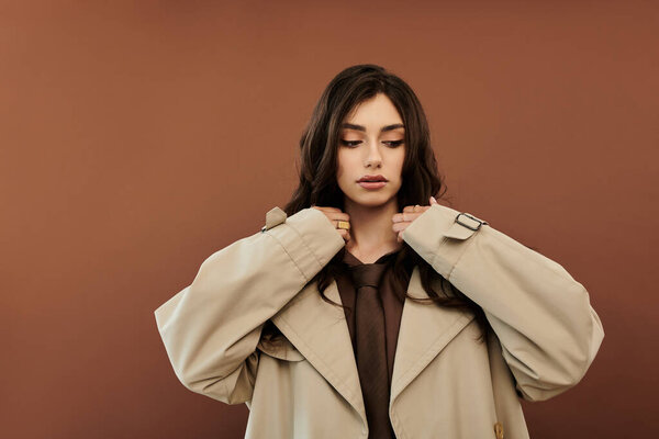 A young and beautiful woman poses elegantly in a stylish autumn outfit against a warm, earthy backdrop.