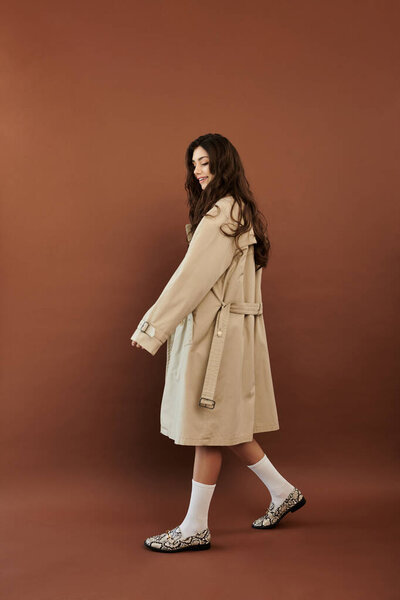 Молодая женщина элегантно позирует в модном осеннем наряде, запечатлевая суть сезонной моды в уютной атмосфере студии.