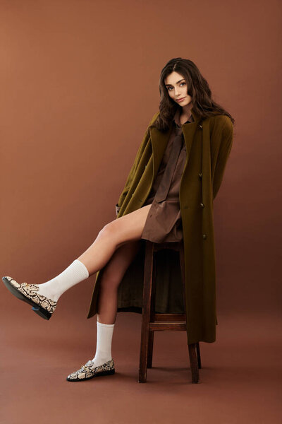Молодая женщина излучает уверенность в модном осеннем наряде, элегантно позируя в теплой студии.