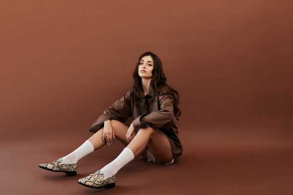 Уверенная в себе молодая женщина изящно позирует, подчеркивая свой модный осенний наряд в теплых, богатых цветах студии.