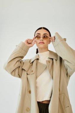 Genç bir kadın zarif bir şekilde sonbahar kıyafeti içinde poz veriyor, minimalist bir stüdyo ortamında sezonun tarzını vurguluyor..