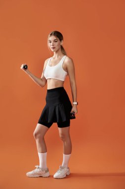 Sporcu bir kadın ağırlıklarla zarifçe poz verirken gücünü gösterir..