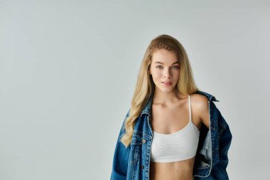 Genç bir kadın zarif bir şekilde duruyor, şık kıyafetine güvenerek yumuşak bir zemine doğru..