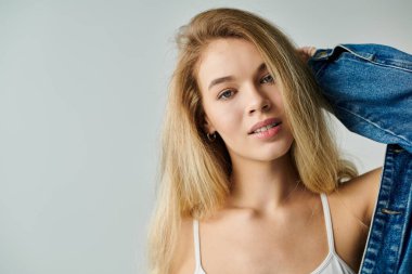 A young woman smiles playfully while posing in a casual, stylish outfit against a light background. clipart