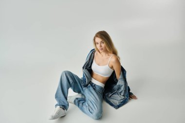 Genç, ışıl ışıl bir kadın, şık bir şekilde yerde oturuyor, sıradan moda ve güven gösterisi yapıyor..