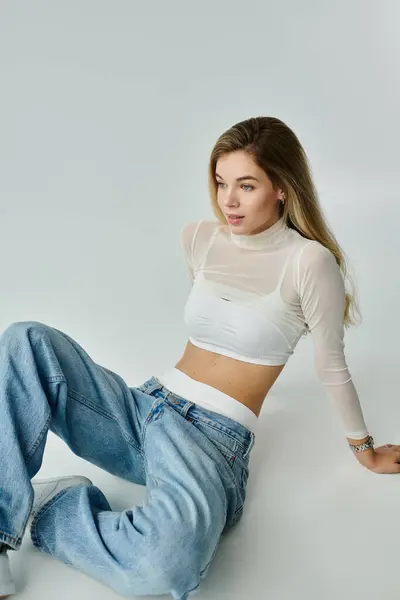 stock image A young woman in a stylish outfit sits on the floor, looking serene and thoughtful in California.