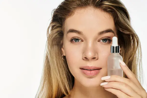 stock image A radiant young woman holds a serum bottle close to her face, showcasing her glowing skin.