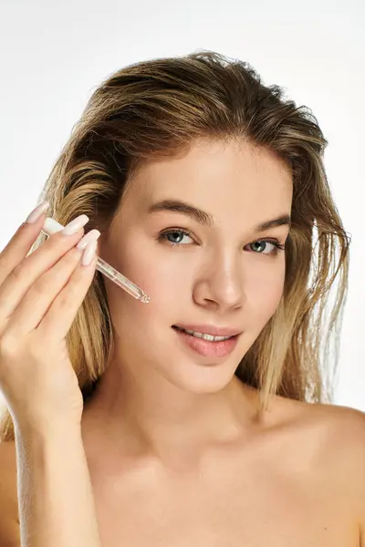 stock image A young woman applies serum to her face, highlighting her radiant skin in soft light.