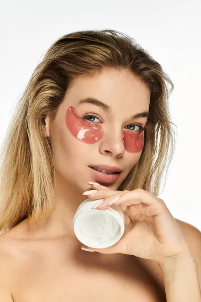 stock image A beautiful young woman applies skincare patches while smiling, embracing self care and beauty.