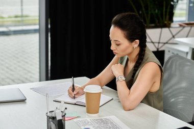 Kendini işine adamış bir profesyonel, ilham verici bir ofis ortamıyla çevrili defterine yazar..
