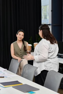 Two professional women share ideas and insights while enjoying coffee in a stylish office. clipart