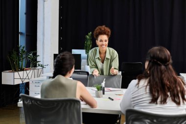 A confident businesswoman leads an engaging discussion at a stylish office work table. clipart