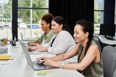 Üç profesyonel kadın laptoplarına odaklanmış şık bir ofiste takım çalışması yapıyorlar..
