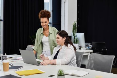 Two professional women engage in a collaborative discussion over a laptop in an office setting. clipart