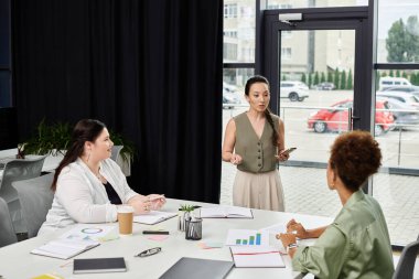Üç profesyonel kadın çağdaş ofis ortamında strateji ve içgörüleri tartışıyor..