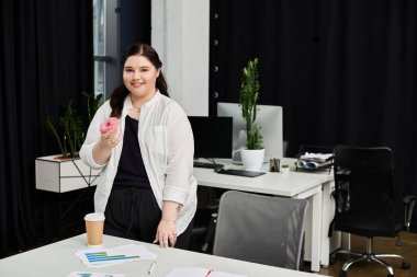 A businesswoman in a stylish outfit takes a break while holding a donut and coffee at her desk. clipart