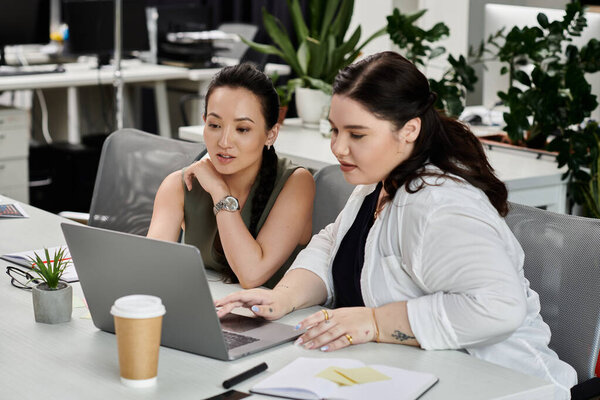 Two professionals engage in a focused discussion while reviewing documents on a laptop.