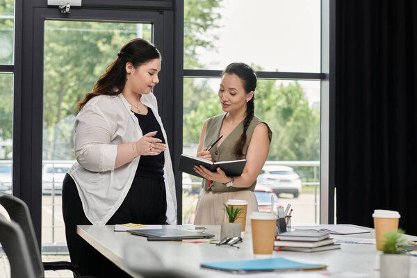 Two professional women engage in a discussion while reviewing notes in a contemporary office.