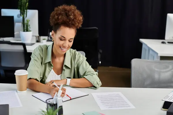 stock image A professional woman smiles as she takes notes in her modern office workspace, radiating focus.