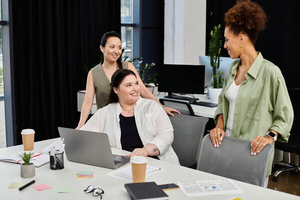 В стильном офисе, три профессиональные женщины участвуют в обсуждении вокруг ноутбука, делясь идеями.
