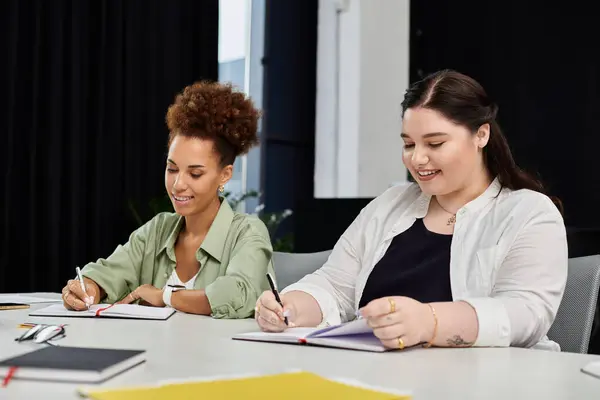 stock image Two professional women collaborate enthusiastically while taking notes at a bright workspace.