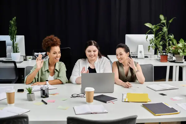 stock image Three professional women are engaged in a lively discussion while working at their office desks.