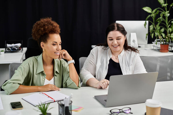 Две стильные деловые женщины участвуют в динамичной дискуссии, рассматривая материалы на ноутбуке.
