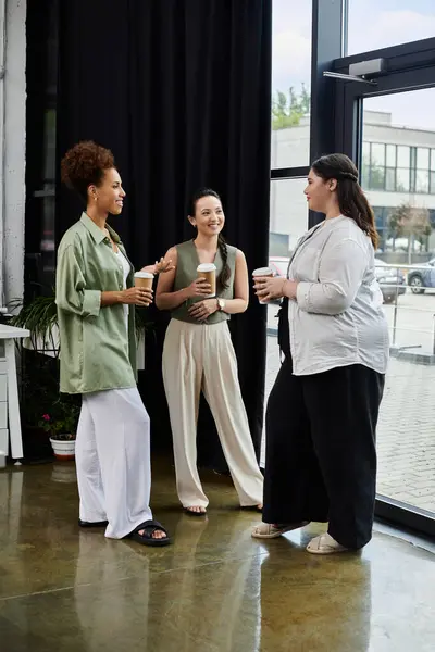 stock image Three stylish professionals engage in lively conversation while sipping coffee in the office.