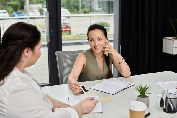 Two professional women discuss ideas while collaborating in a stylish office setting.
