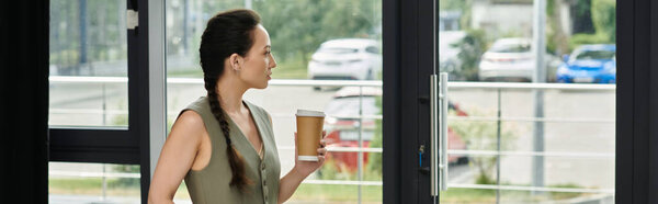 Уравновешенная деловая женщина стоит у окна, наслаждаясь кофе, пока она готовится к своим заданиям.