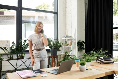 Canlı bir ofiste, bitkilerle çevrili neşeli genç bir profesyonel telefonda konuşuyor..